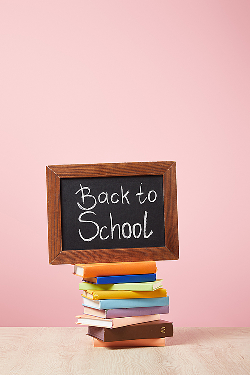 stack of books with chalkboard with back to school lettering isolated on pink