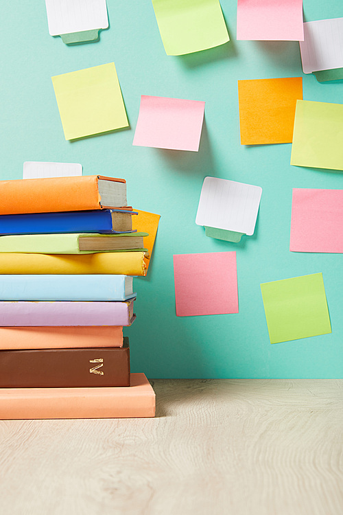 stack of books on table near multicolored sticky notes on turquoise wall