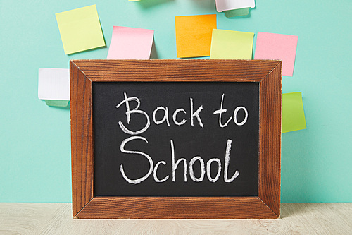 chalkboard with back to school lettering near multicolored sticky notes on turquoise wall