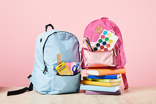 blue and pink backpacks with school supplies near books isolated on pink