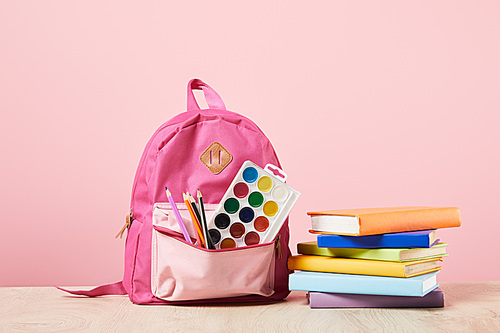 pink backpack with supplies in pocket near colorful books isolated on pink