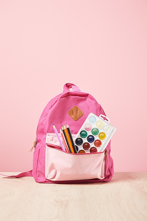 pink backpack with supplies in pocket isolated on pink