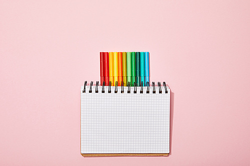 top view of multicolored felt pens near blank notebook isolated on pink