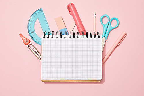 top view of blank notebook among school supplies on pink background