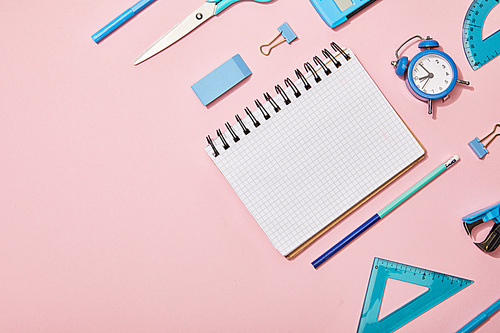 flat lay with blue school supplies and blank notebook isolated on pink