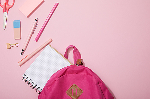 top view of scattered school supplies and blank notebook near backpack isolated on pink