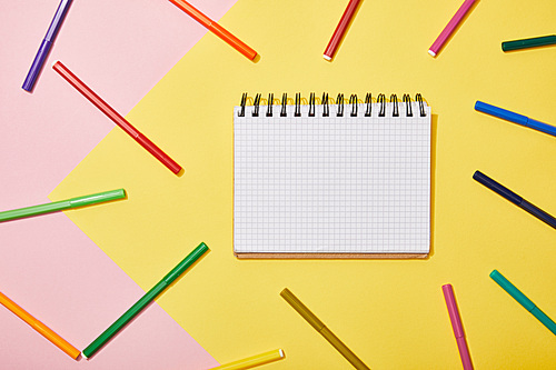 top view of blank notebook with multicolored felt pens on pink and yellow background
