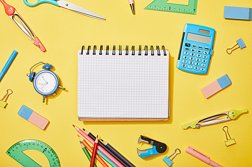 top view of blank notebook among school supplies on yellow background