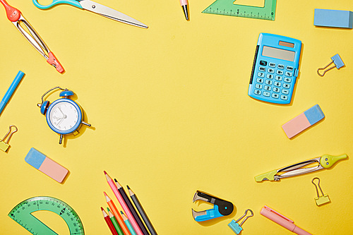 top view of school supplies scattered on yellow background with copy space
