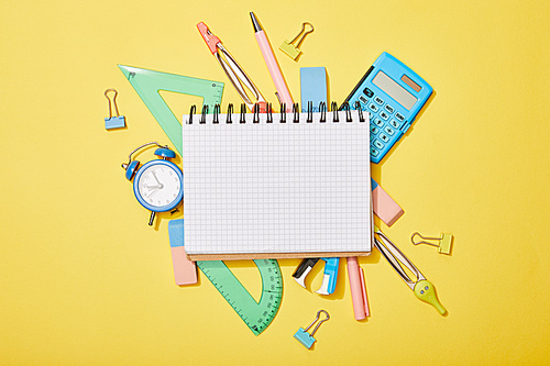 top view of school supplies scattered on yellow background with empty notebook