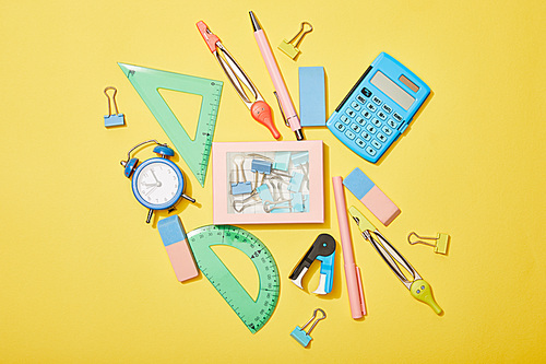 top view of school supplies scattered near box with clips on yellow background