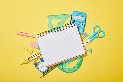 top view of school supplies scattered on yellow background with blank notebook