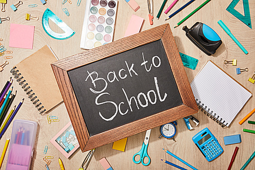 top view of various school supplies and chalkboard with back to school lettering on wooden desk