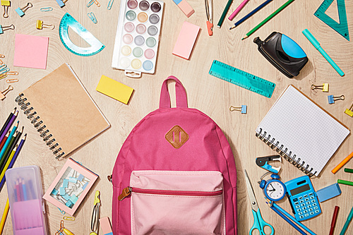 top view of various school supplies with pink backpack on wooden desk