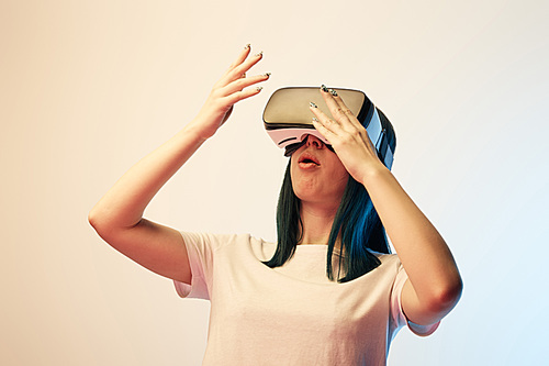 surprised young woman wearing virtual reality headset  and gesturing on beige and blue