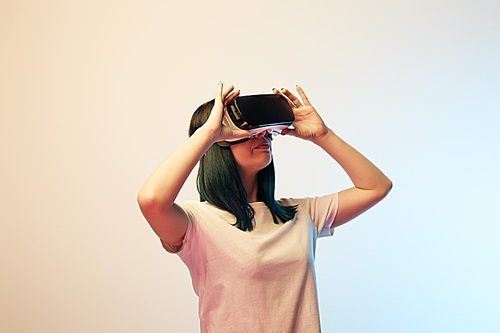 attractive young woman touching virtual reality headset on beige and blue