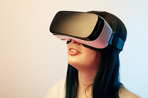 cheerful brunette girl wearing virtual reality headset on beige and blue
