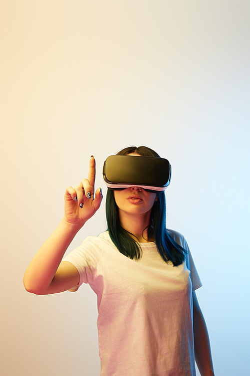 selective focus of woman pointing with finger while wearing virtual reality headset on beige and blue