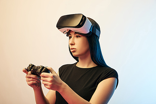 KYIV, UKRAINE - APRIL 5, 2019: Attractive brunette woman playing video game while wearing virtual reality headset on beige and blue