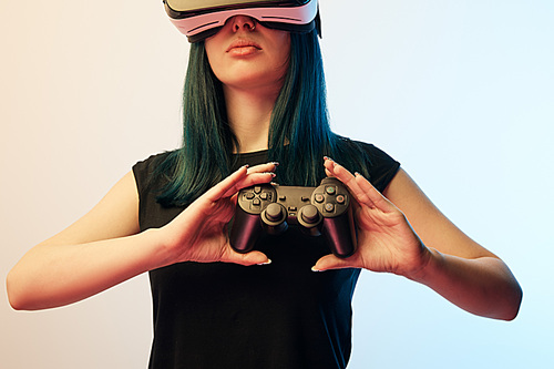 KYIV, UKRAINE - APRIL 5, 2019: Cropped view of brunette woman holding joystick while wearing virtual reality headset on beige and blue