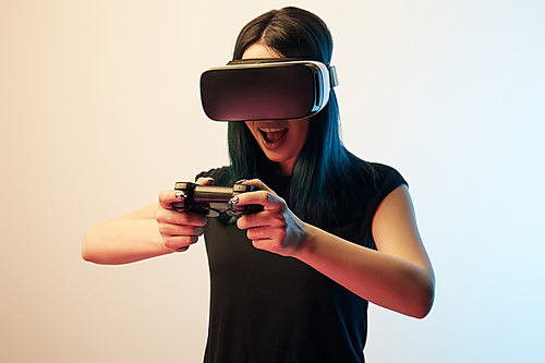 KYIV, UKRAINE - APRIL 5, 2019: Cheerful brunette woman playing video game while wearing virtual reality headset on beige and blue
