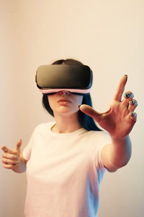 selective focus of brunette young woman in virtual reality headset gesturing on beige