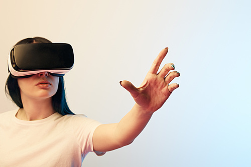 selective focus of young woman in virtual reality headset gesturing on beige and blue