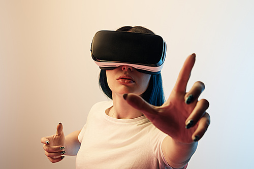 selective focus of brunette woman wearing virtual reality headset and gesturing on beige and blue