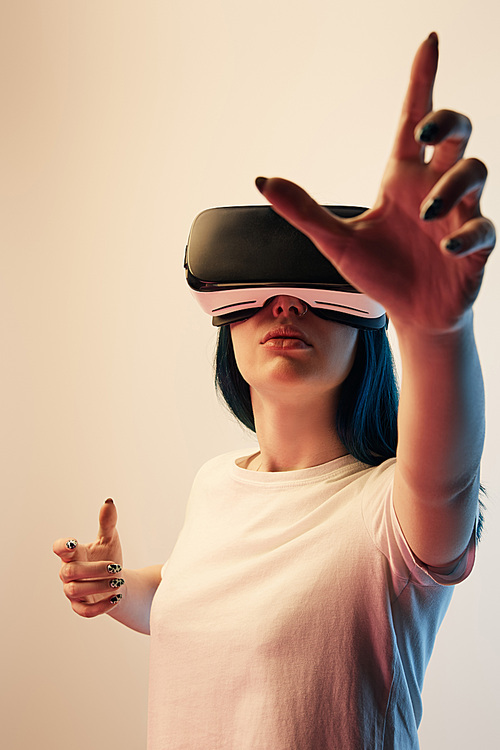selective focus of brunette girl wearing virtual reality headset and gesturing on beige