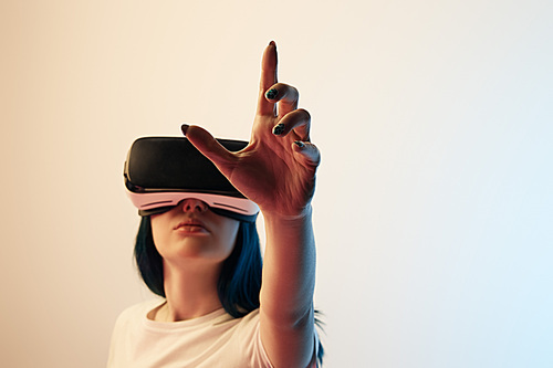 selective focus of brunette girl wearing virtual reality headset and gesturing on beige and blue