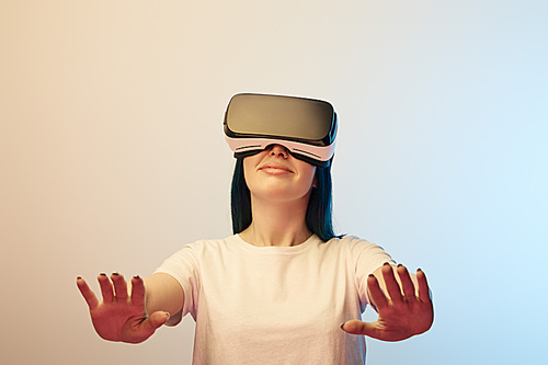 selective focus of happy young  woman in virtual reality headset gesturing on beige and blue