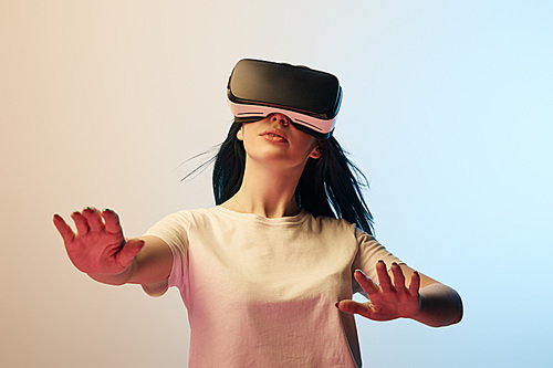 selective focus of girl in white t-shirt wearing virtual reality headset and gesturing on beige and blue