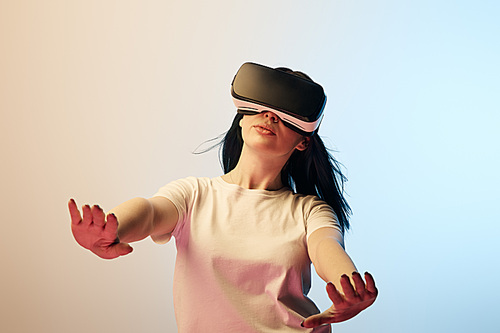 selective focus of woman in white t-shirt wearing virtual reality headset and gesturing on beige and blue