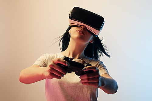 KYIV, UKRAINE - APRIL 5, 2019: Selective focus of woman in white t-shirt wearing virtual reality headset and holding joystick on beige and blue