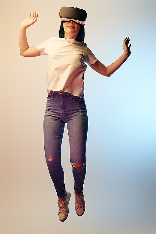 cheerful woman in virtual reality headset levitating and gesturing on beige and blue