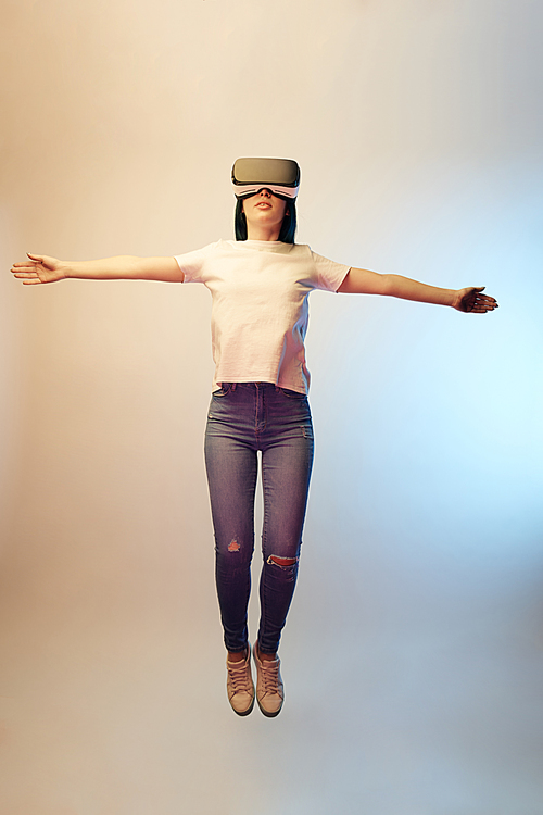 young woman in virtual reality headset with outstretched hands levitating on beige and blue