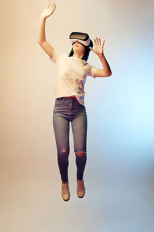 young woman in virtual reality headset gesturing while levitating on beige and blue