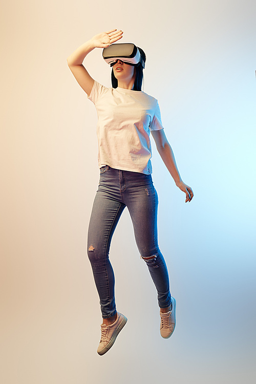 brunette young woman in virtual reality headset levitating and gesturing on beige and blue