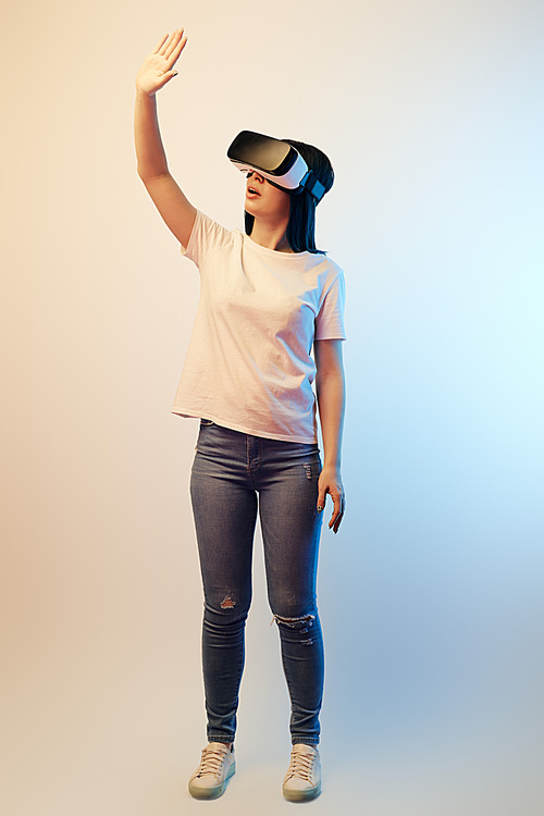 brunette young woman in virtual reality headset standing and gesturing on beige and blue