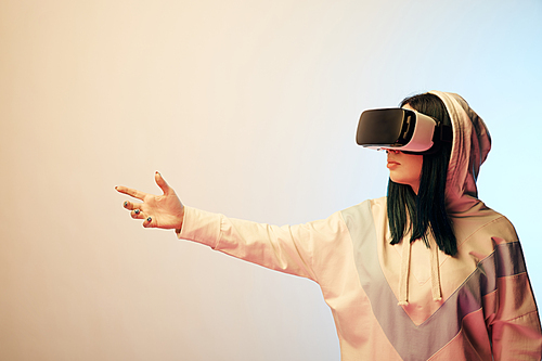 young brunette girl wearing virtual reality headset and gesturing on beige and blue