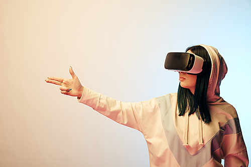 brunette girl wearing virtual reality headset and gesturing on beige with gradient