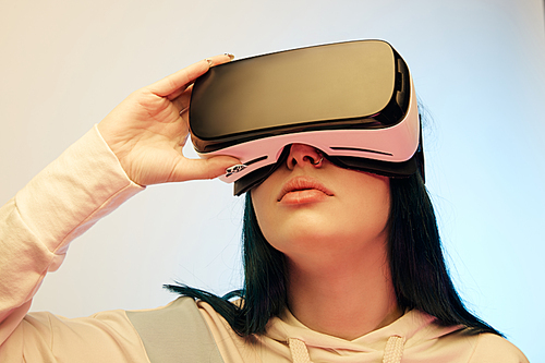 low angle view of brunette woman touching virtual reality headset on beige and blue