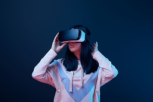 young brunette woman touching virtual reality headset on blue