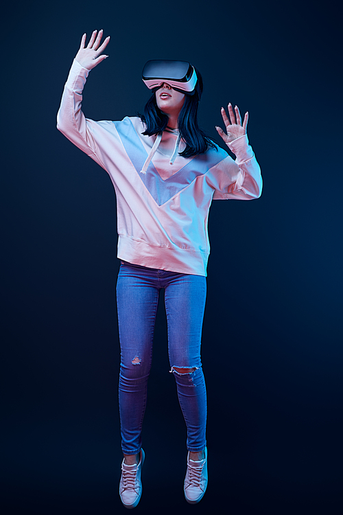 brunette young woman gesturing while wearing virtual reality headset on blue