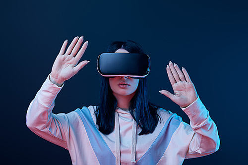 young brunette woman wearing virtual reality headset and gesturing on blue