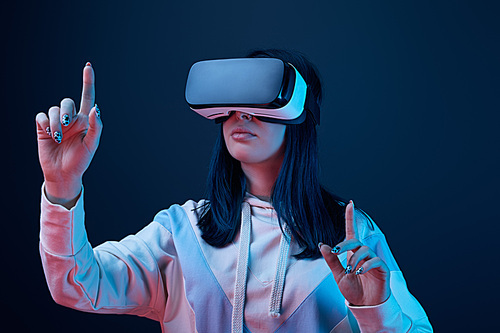 selective focus of young woman wearing virtual reality headset and pointing with fingers on blue