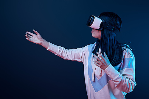 brunette girl wearing virtual reality headset and gesturing on blue