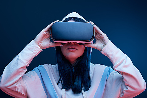 brunette girl in hood touching virtual reality headset on blue