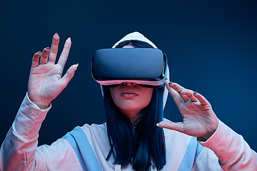 brunette girl in hood gesturing while virtual reality headset on blue