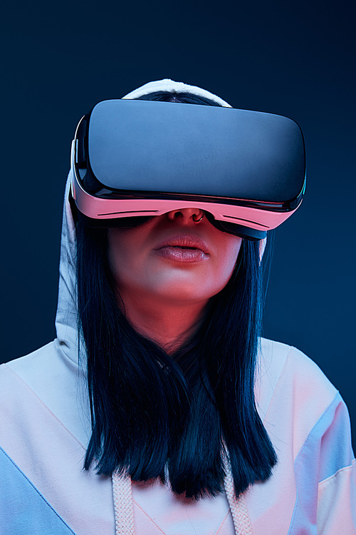 low angle view of brunette young woman in hood using virtual reality headset on blue